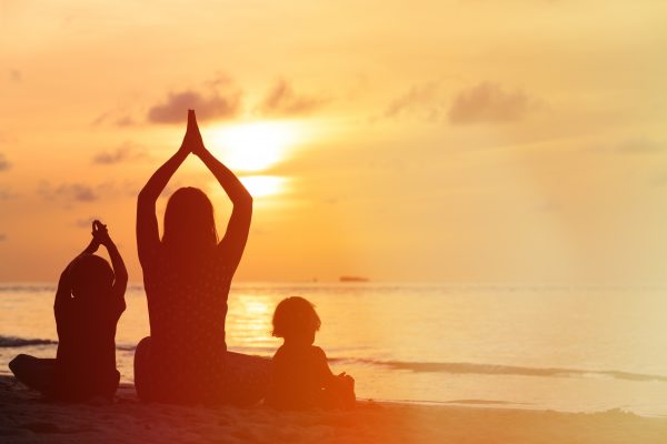 silhouette of mother and kids doing yoga at sunset sea